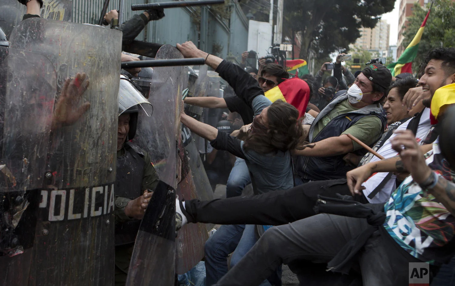 Opponents of President Evo Morales kick the shields of police guarding the electoral court, during a national strike in La Paz, Bolivia, Thursday, Dec. 6, 2018. Bolivian city's were semi-paralyzed by a Thursday strike called by opposition groups a day after the country's top electoral court announced that it accepted Morales' candidacy for a fourth term in office, despite a constitutional ban and referendum against such a re-election. (AP Photo/Juan Karita)
