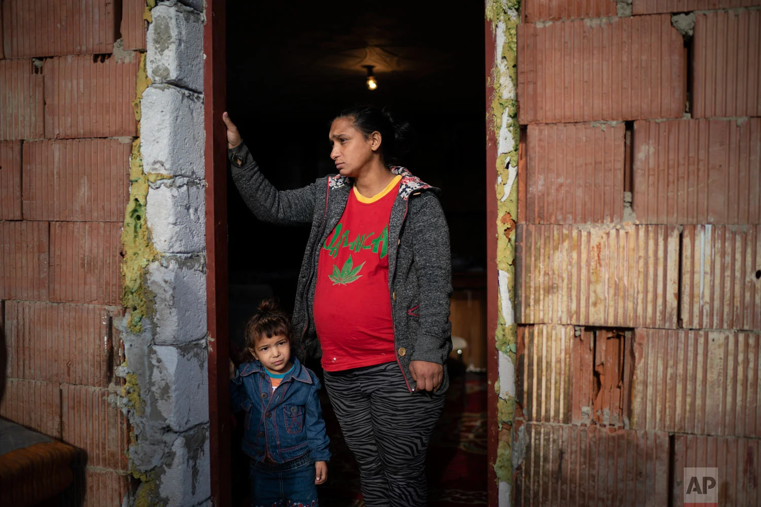 Jarmila Noskova, 33, stands at the entrance of her house with her daughter on Nov. 14, 2018, in Podhorany village near Kezmarok, Slovakia. Noskova, a Roma woman now pregnant with her seventh child, said she cried for days every time she was forced to remain in the hospital after birth, terrified the hospital would alert the police if she left. (AP Photo/Felipe Dana)