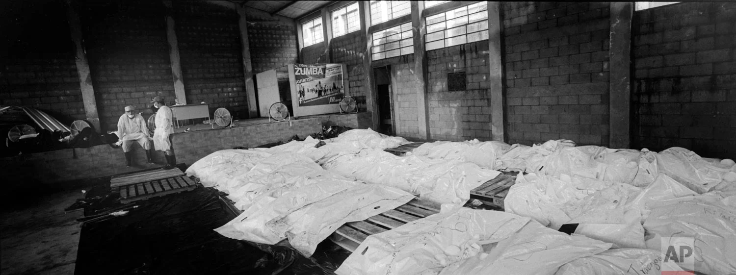 A forensic worker stands while another rests next to body bags containing the remains of victims of the Volcan de Fuego, or Volcano of Fire, eruption, in a cinderblock warehouse converted into a makeshift morgue on June 8, 2018, in Escuintla, Guatemala. (AP Photo/Rodrigo Abd)