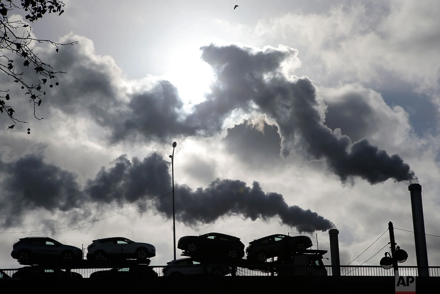 In this Friday, Nov. 30, 2018 photo, smoke rises from a factory as a truck loaded with cars crosses a bridge in Paris, France. (AP Photo/Michel Euler)