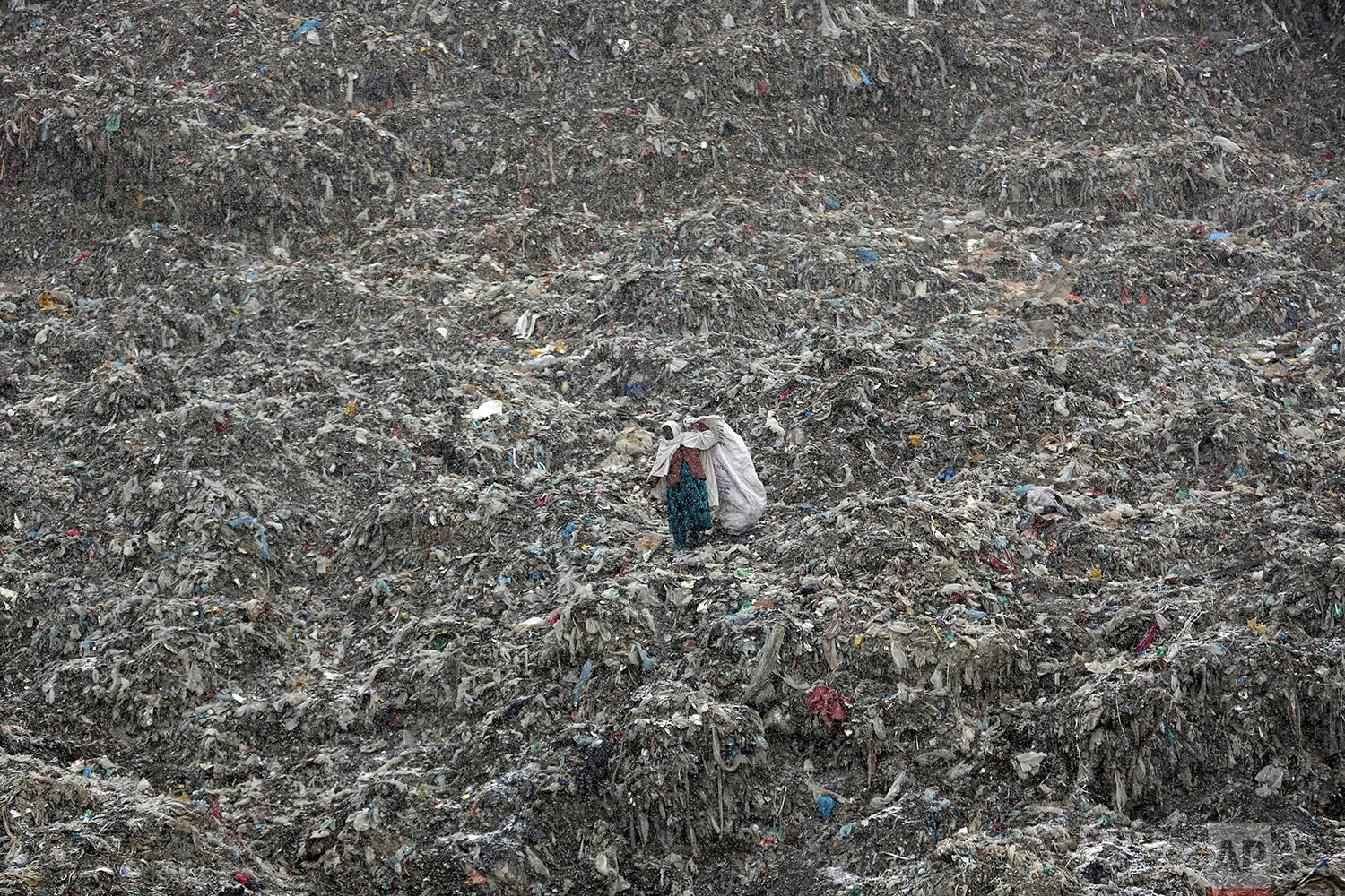 In this Tuesday, Dec. 11, 2018 photo a woman who scavenges recyclable materials from garbage for a living walks across a mountain of garbage at the dump on the outskirts of Kabul, Afghanistan. (AP Photo/Massoud Hossaini)