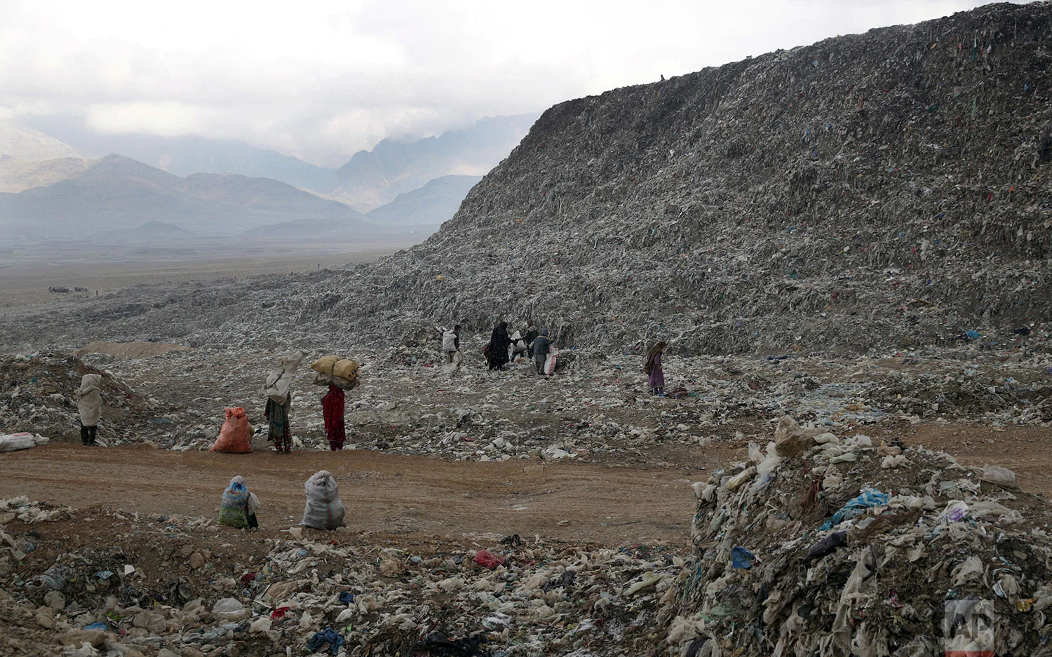 In this Tuesday, Dec. 11, 2018 photo, people, who scavenge recyclable materials from garbage for a living, walk near a mountain of garbage at the dump on the outskirts of Kabul, Afghanistan. (AP Photo/Massoud Hossaini)