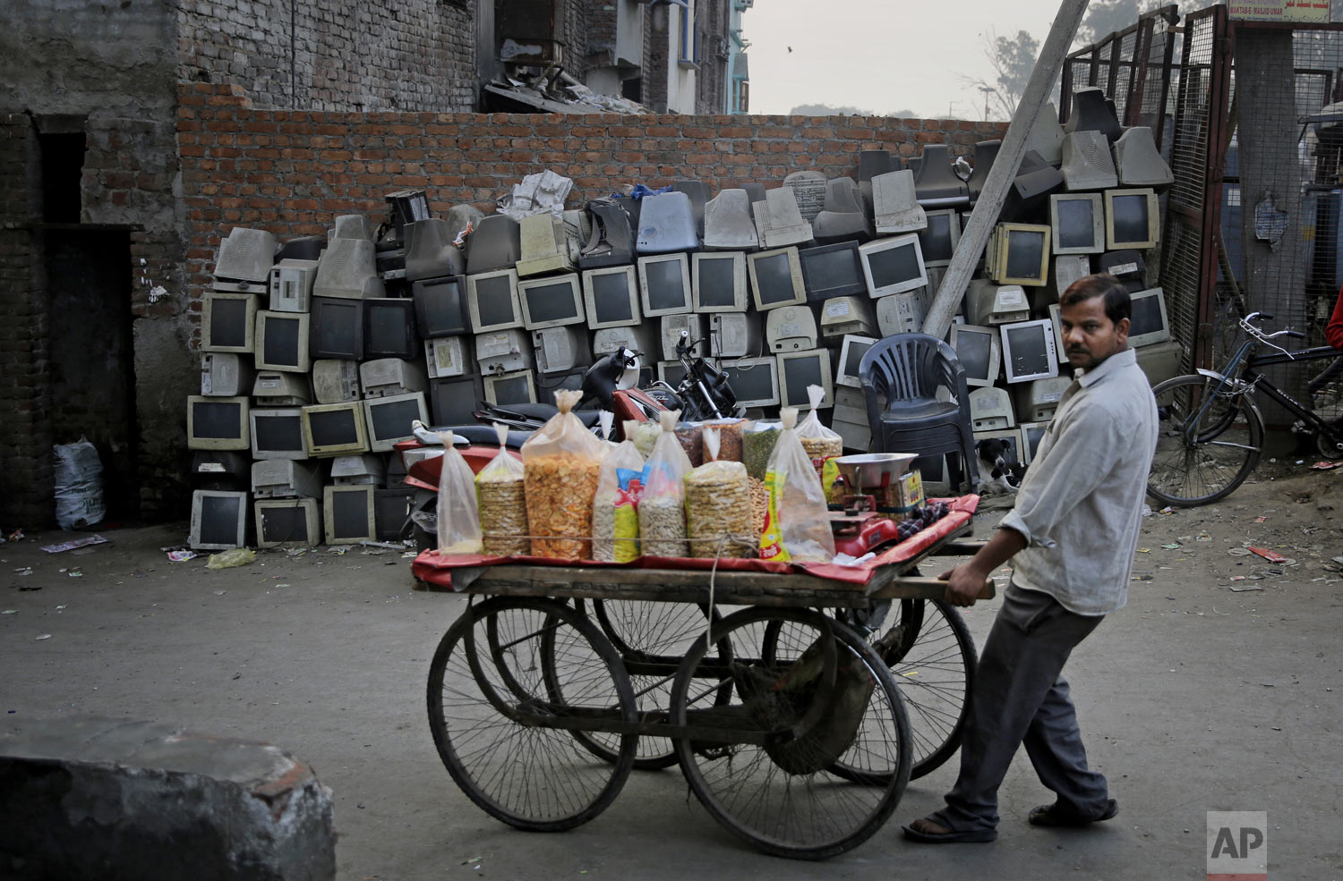  A snack vendor pushes his cart past discarded computer monitors stacked next to a wall on the side of a road in New Delhi, India, on Saturday, Dec. 8, 2018. (AP Photo/Altaf Qadri) 