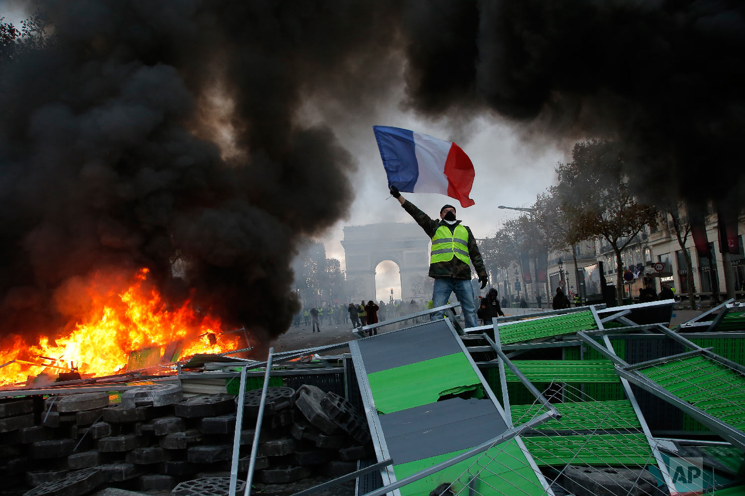  A demonstrator waves the French flag onto a burning barricade on the Champs-Elysees avenue during a demonstration against the rising of the fuel taxes in Paris on Nov. 24, 2018. (AP Photo/Michel Euler) 