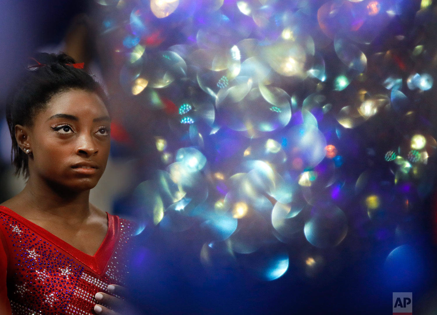  New world champion Simone Biles of the U.S. waits for the medal ceremony as the light bounces off a Russian gymnasts suit after the women's team final of the Gymnastics World Chamionships at the Aspire Dome in Doha, Qatar on Oct. 30, 2018. (AP Photo