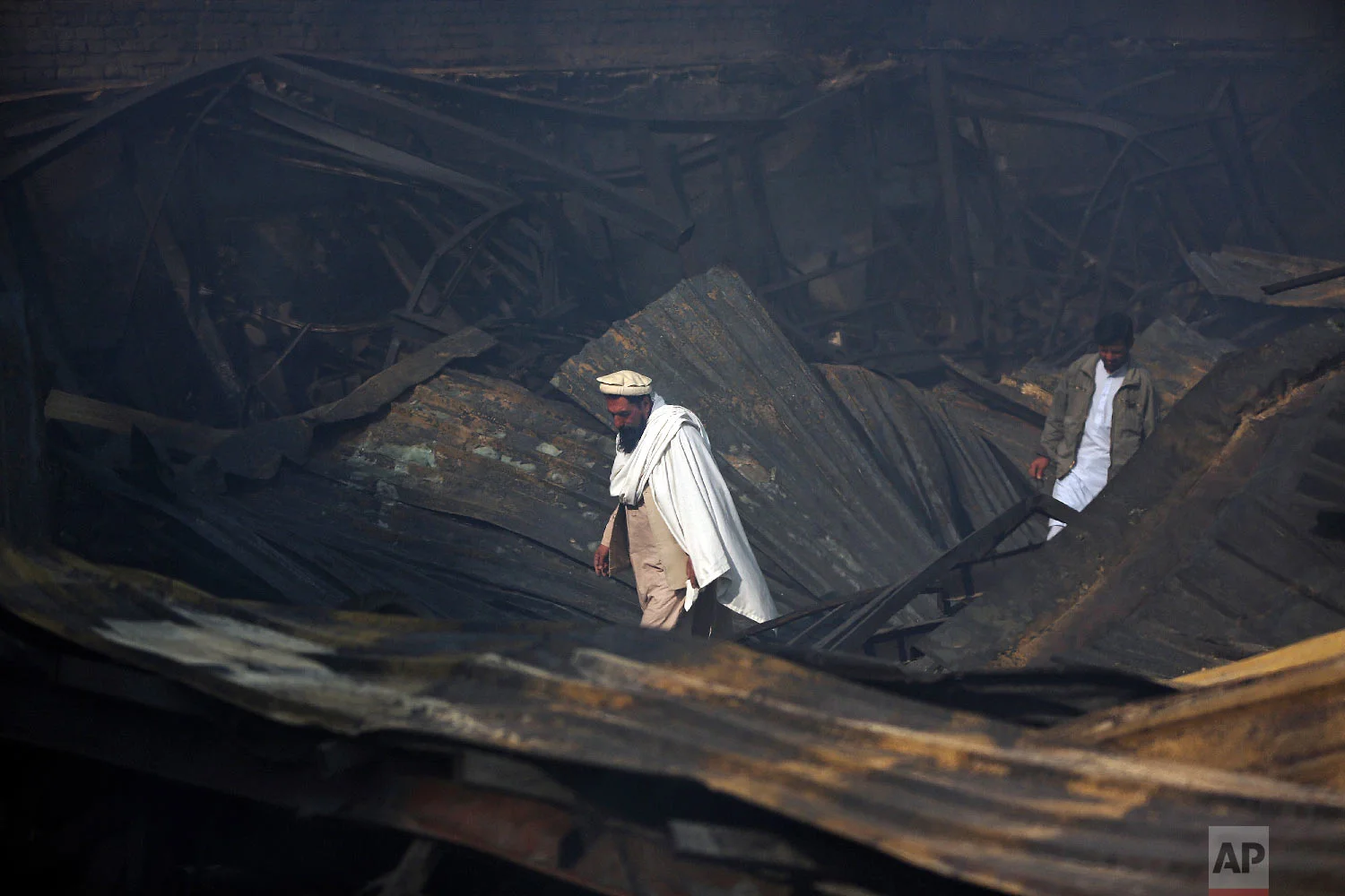 Men walk among the ruins after a fire devastated an electronic appliances market, in Kabul, Afghanistan, Nov. 2, 2018. (AP Photo/Massoud Hossaini)