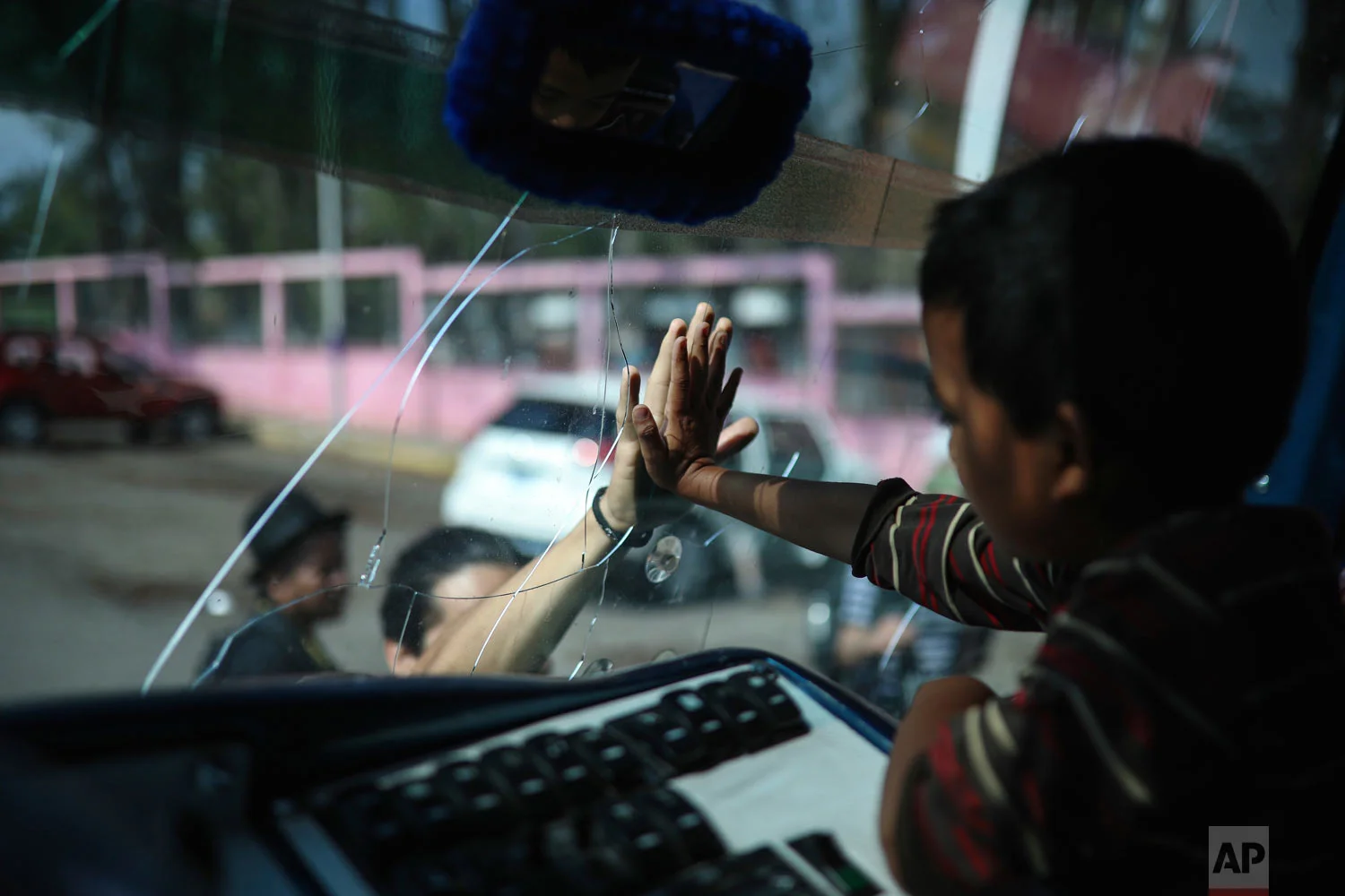 In this April 5, 2018 photo, a migrant says goodbye to a friend through the windshield of a bus that will carry him to the capital from Matias Romero, Oaxaca state, Mexico where Central American migrants with the annual "Stations of the Cross" caravan camped out. The Easter-season caravans have been held annually for about 10 years to draw attention to the plight of migrants, but was never equipped to march all the way to the US. (AP Photo/Felix Marquez)