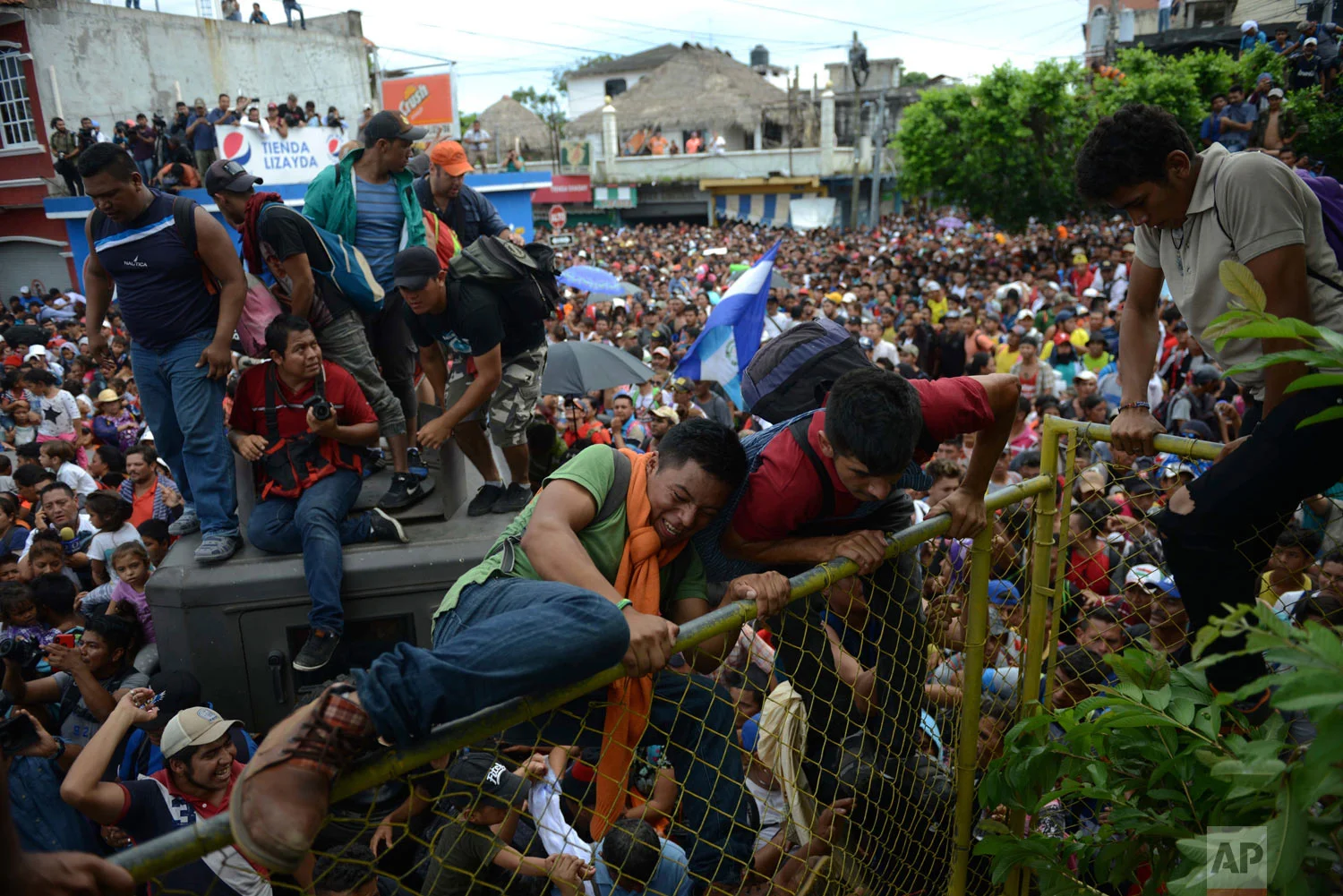 In this Oct. 19, 2018 photo, Central American migrants traveling in a caravan rush across Guatemala's border with Mexico in Tecun Uman, Guatemala. After arriving at the fence, some climbed atop it and on U.S.-donated military jeeps, finally succeeding in tearing down the barrier. (AP Photo/Oliver de Ros)