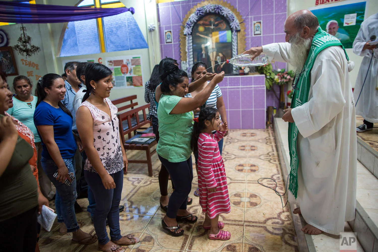 In this Jan. 14, 2018 photo, Father Pablo Zabala, affectionately known as "Padre Pablo," squirts holy water from a water bottle during his last Mass as the parish priest in Boca Colorado, in Peru's Madre de Dios region in the Amazon. Zabala first traveled to the Amazon in 1978 as a young biologist collecting butterflies and condors for his university’s museum in Spain. He returned to Peru years later to work in the Amazon as a priest. (AP Photo/Rodrigo Abd)