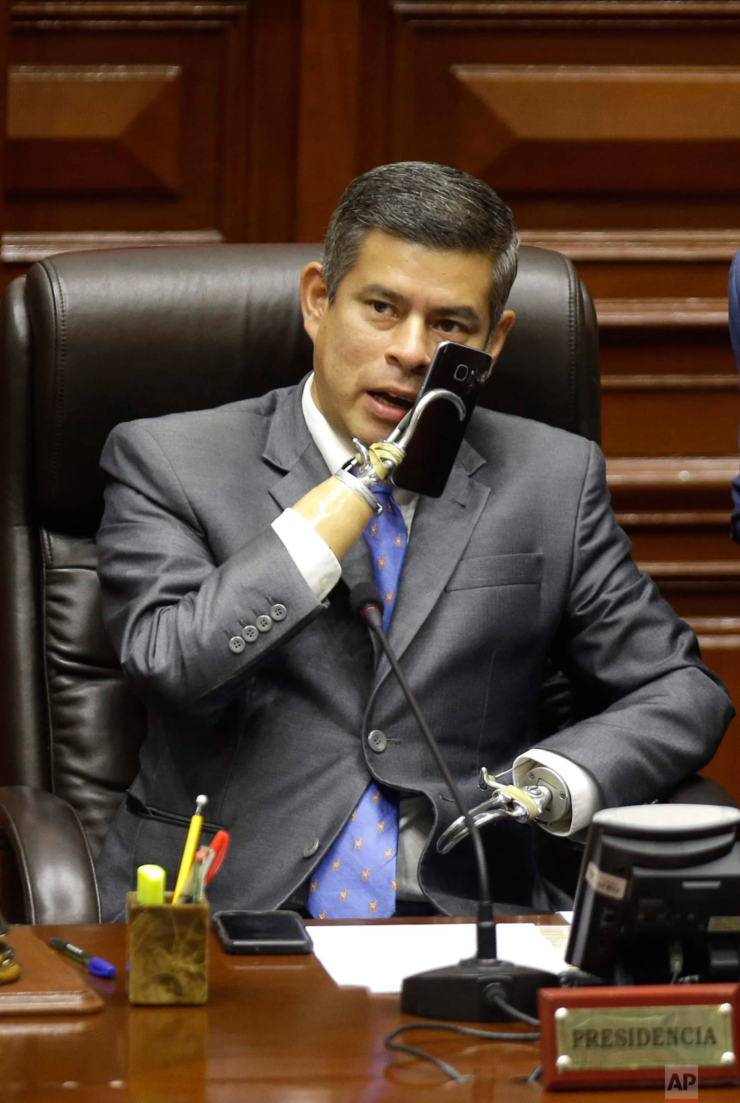 In this March 22, 2018 photo, Congress President Luis Galarreta, who was born without arms, speaks on his cell before the start of a debate on the resignation of Peru's President Pedro Pablo Kuczynski in Lima, Peru. Kuczynski offered his resignation ahead of the impeachment vote, after damaging leaks of confidential documents raised doubts about his integrity and made it impossible to govern. (AP Photo/Martin Mejia)