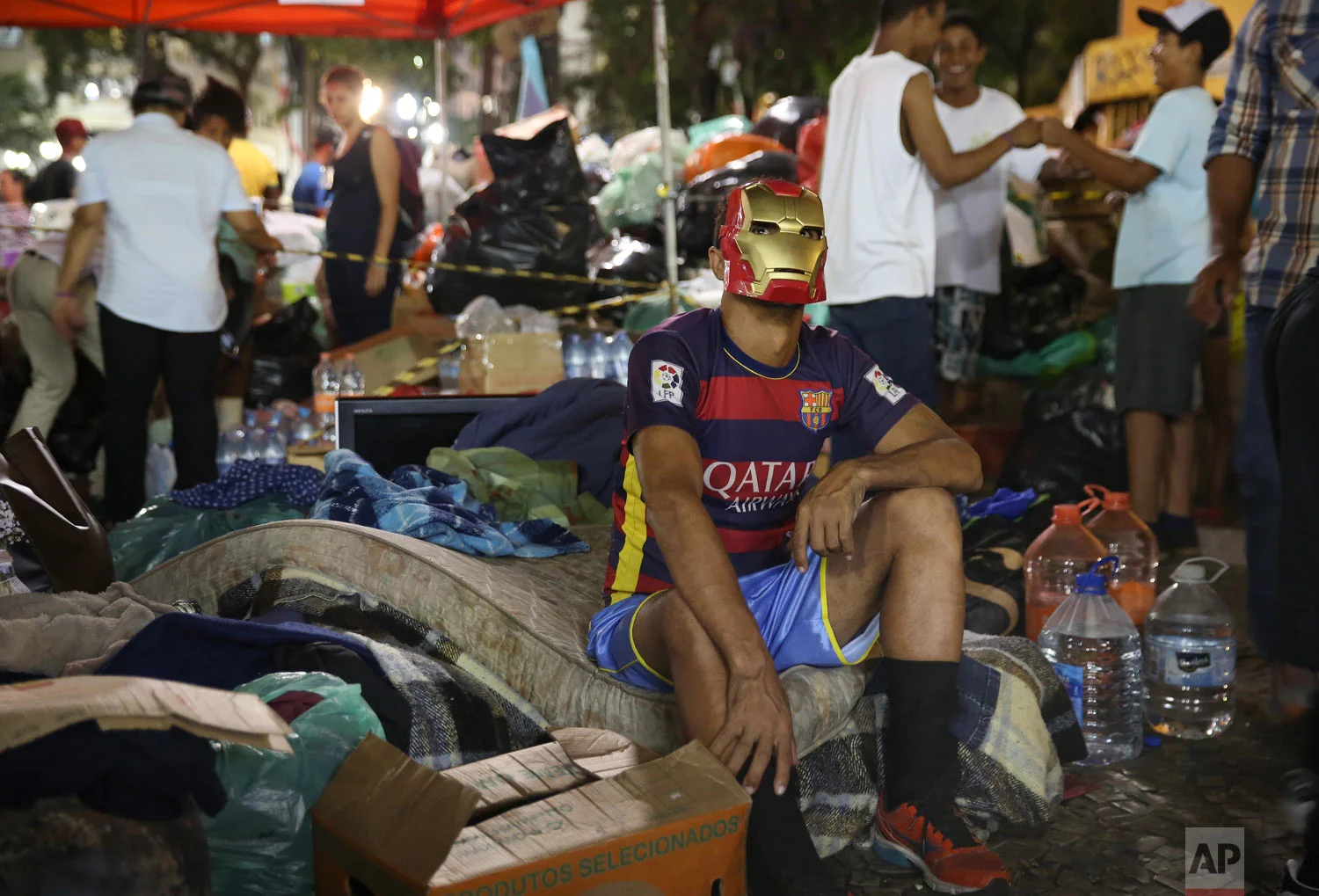 In this May 3, 2018 photo, a masked man sits outside on his belongings after the building he was living in with other squatters burned down, triggered by a short circuit, in downtown Sao Paulo, Brazil. Tens of thousands of working class families in Sao Paulo can't afford to rent an apartment and high transportation costs render low-rent places on the city's outskirts unaffordable. (AP Photo/Andre Penner)