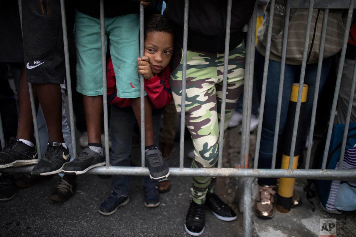 In this May 23, 2018 photo, a boy squeezes between people's legs as he waits outside the Granja Comary training center for a chance to see Brazil's national soccer team in Teresopolis, Brazil. (AP Photo/Leo Correa)