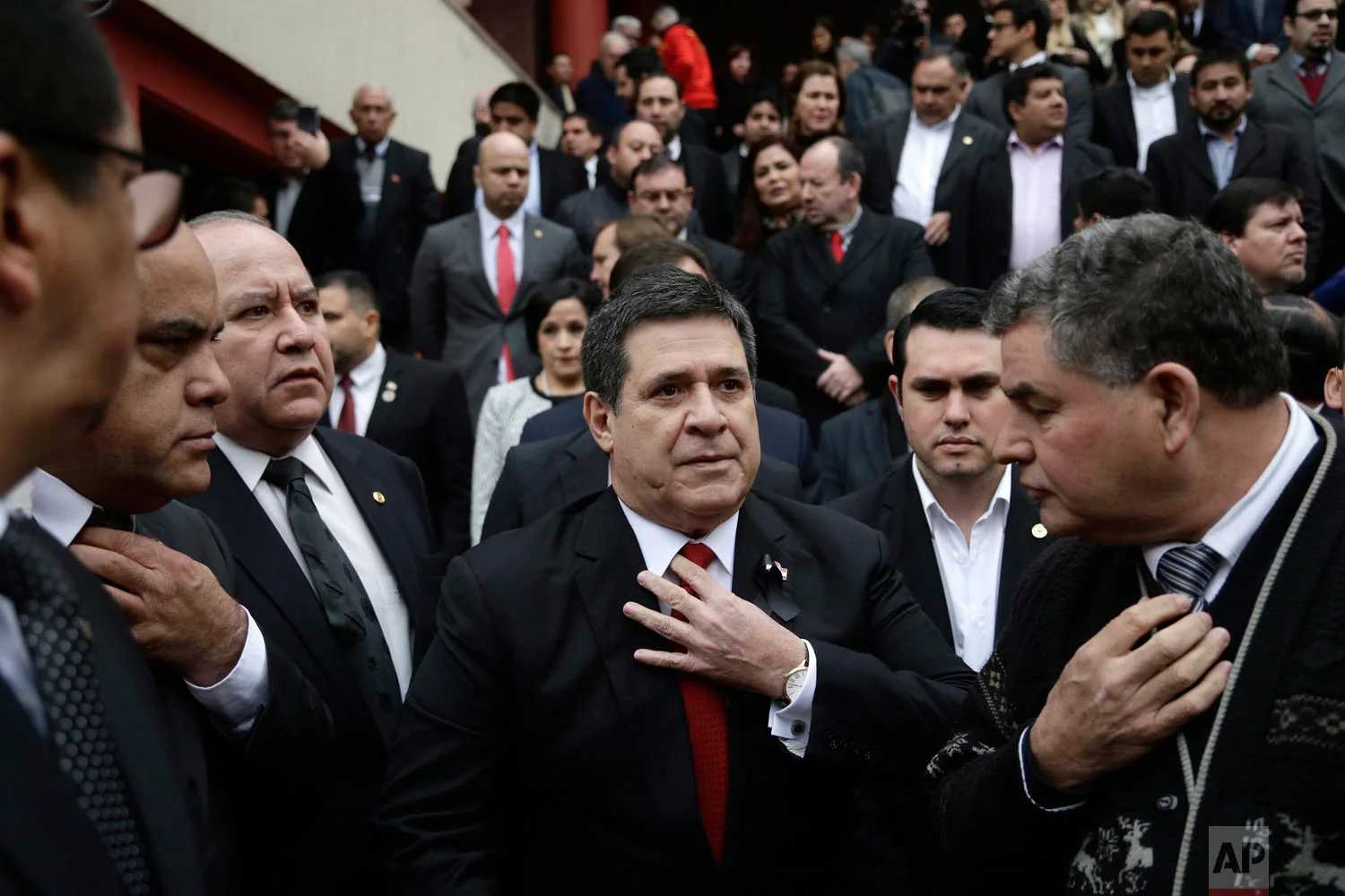 In this July 27, 2018 photo, Paraguay's President Horacio Cartes straightens his tie as he waits for the arrival of the coffin of his Agriculture Minister Luis Gneiting for a memorial service in Asuncion, Paraguay. The minister and three other people died when the twin-engine plane they were traveling in went down shortly after taking off at night. (AP Photo/Jorge Saenz)