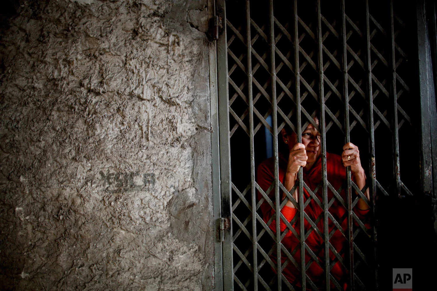 In this Sept. 6, 2018 photo, Modesta Cabanas stands behind her home's security gate on the outskirts of Buenos Aires, Argentina. Cabanas feeds her family at a soup kitchen, and says that since Argentina's economic crisis started, the portions are much smaller because more people are eating there. (AP Photo/Natacha Pisarenko)