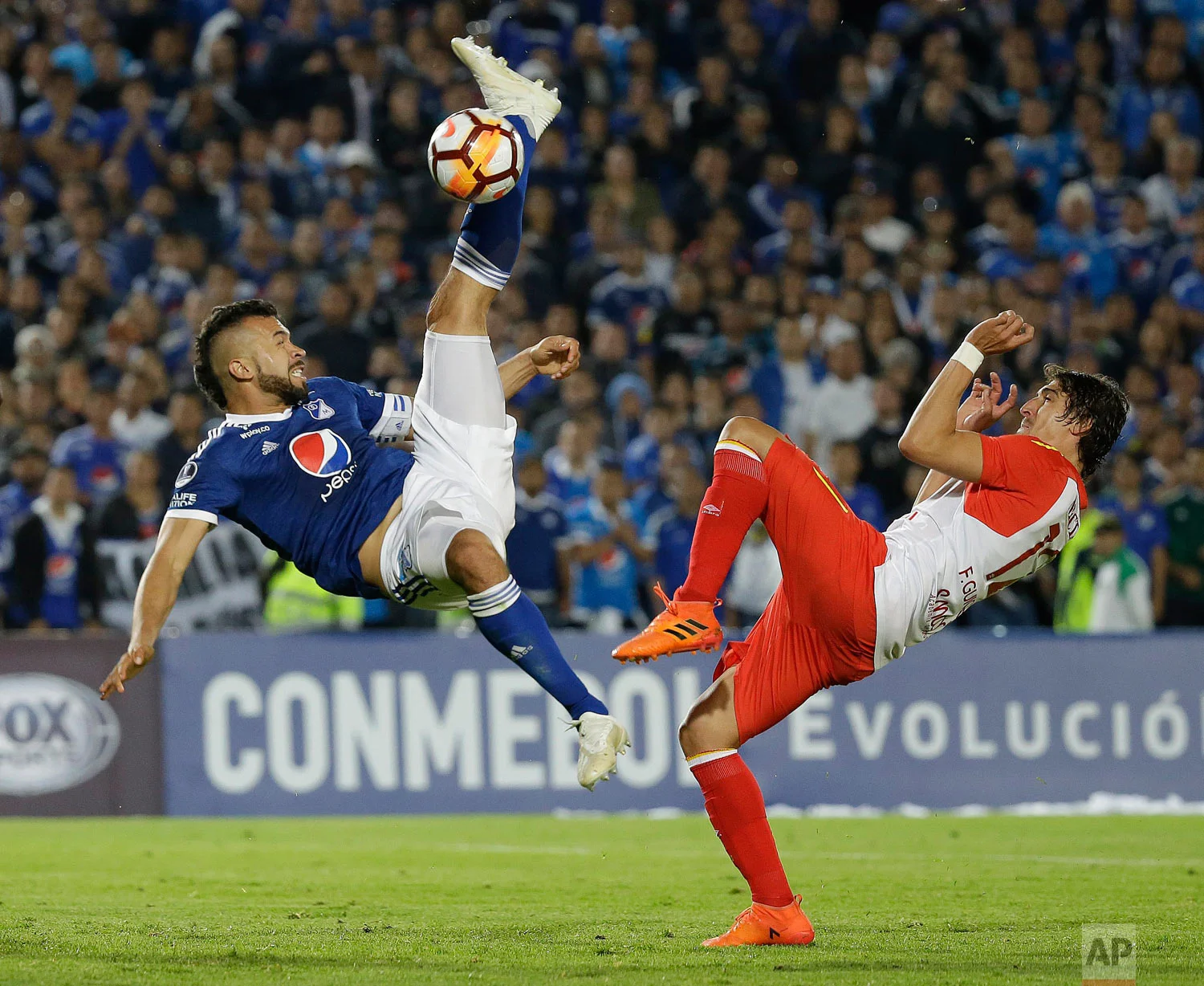 In this Oct. 2, 2018 photo, Andres Cadavid of Colombia's Millonarios kicks the ball past Facundo Guichon of Colombia's Independiente Santa Fe during a Copa Sudamericana soccer match in Bogota, Colombia. (AP Photo/Fernando Vergara)