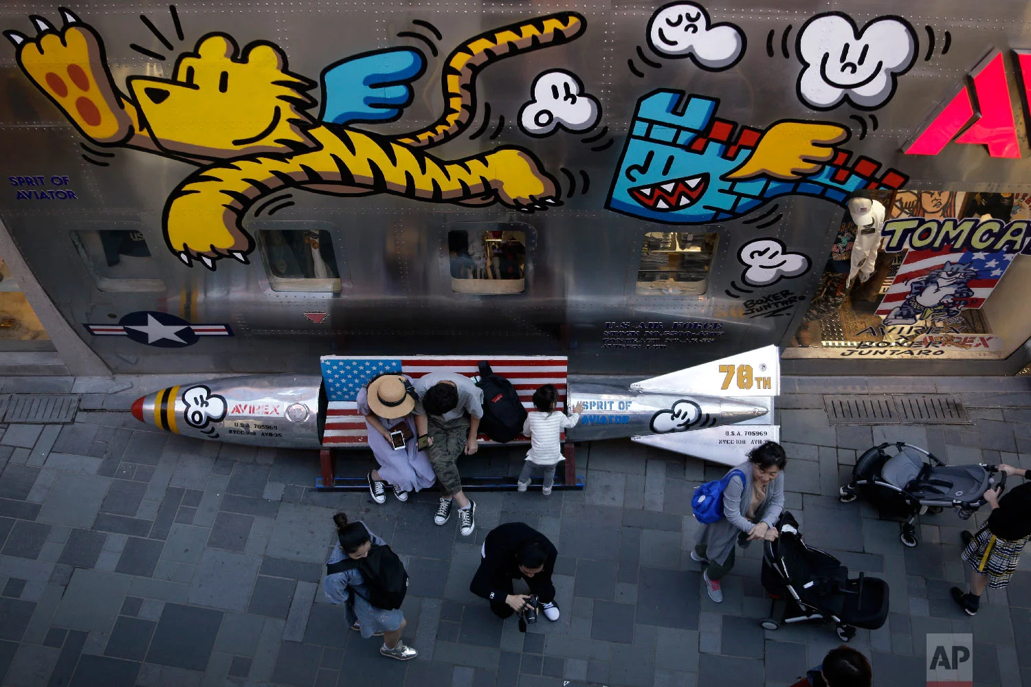 Shoppers spend their time near a bench in a shape of a mocked aerial bomb and a U.S. flag outside a fashion boutique selling U.S. brand clothing at the capital city's popular shopping mall in Beijing, Monday, Sept. 24, 2018. China raised tariffs Monday on thousands of U.S. goods in an escalation of its fight with President Donald Trump over technology policy and accused Washington of bullying Beijing and damaging the global economy. (AP Photo/Andy Wong)