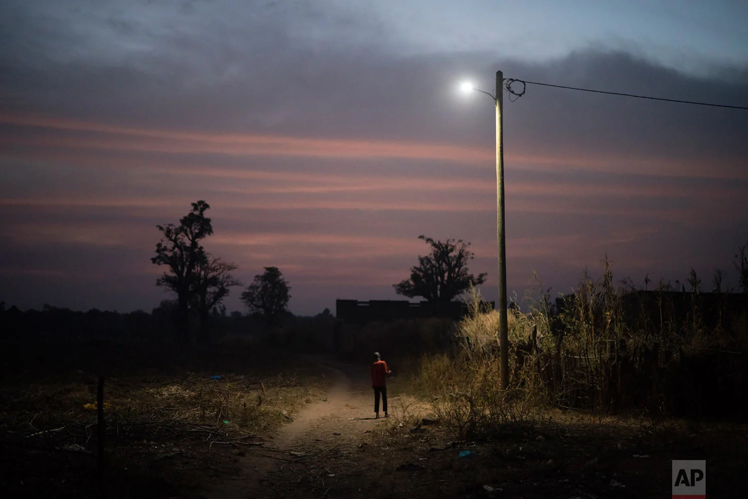 A boy stand under a street lamp at dusk on Nov. 26, 2018, in a village near Goudiry, Senegal. (AP Photo/Felipe Dana)