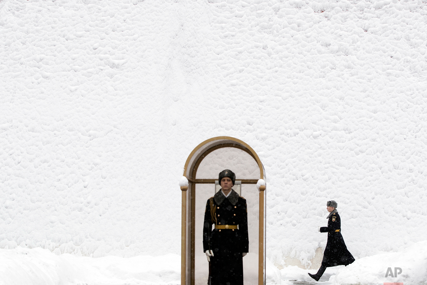 An Honor guard soldier walks along the Kremlin Wall, covered by snow, as his fellow soldier stands at the Tomb of Unknown Soldier in Moscow, Russia, Wednesday, Jan. 31, 2018. (AP Photo/Pavel Golovkin)