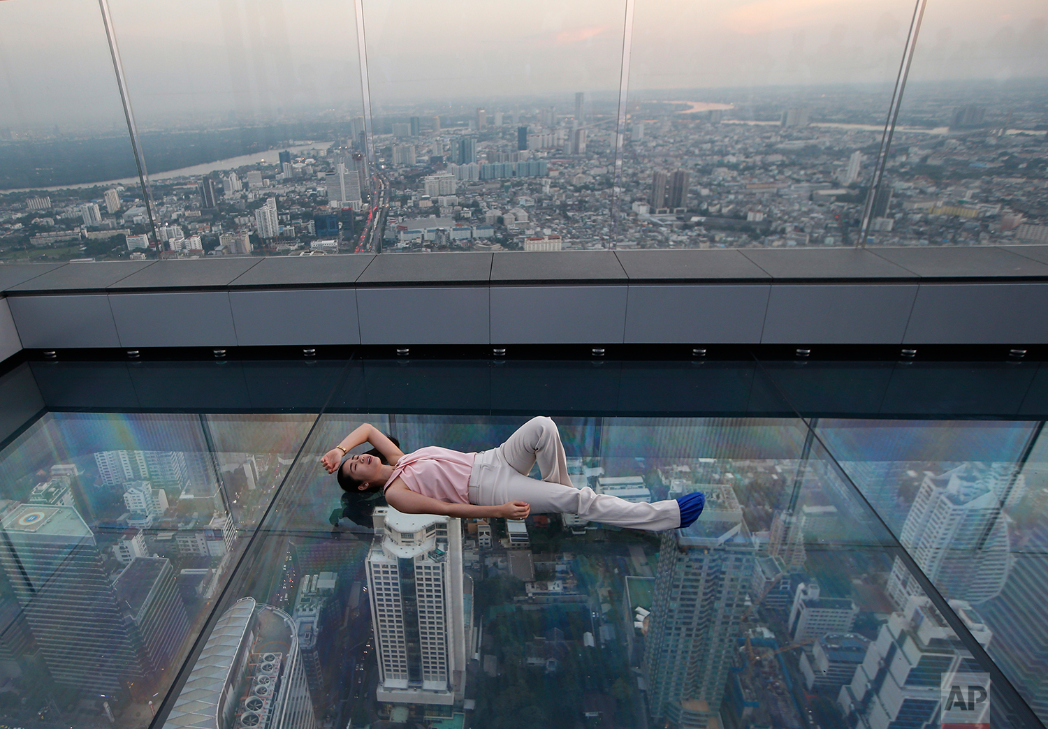 In this Nov. 21, 2018, photo, a woman lies on the glass bottom deck of the King Power Mahanakhon building high above Bangkok, Thailand. The King Power Mahanakhon building, currently Thailand's tallest at 314 meters (1,030 feet) with 78 floors, has a 360-degree view of Bangkok. (AP Photo/Sakchai Lalit, File)