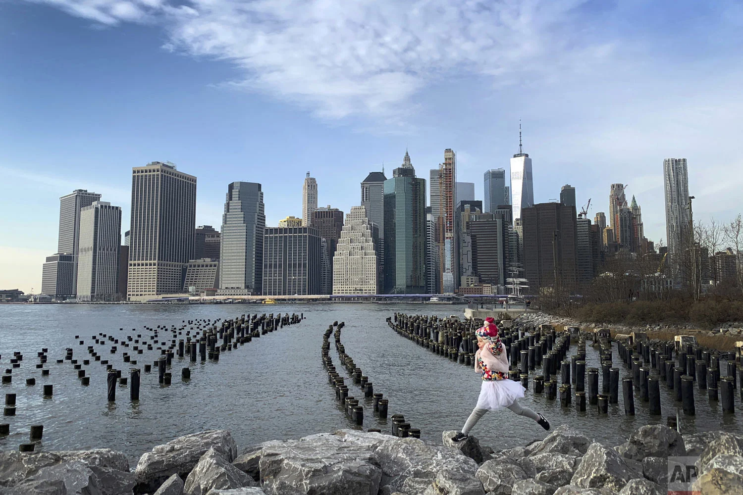 With downtown Manhattan in the background, a girl leaps across boulders forming a breakwater along the Brooklyn Bridge Park on Thursday Dec. 27, 2018, in the Brooklyn borough of New York. (AP Photo/Wong Maye-E)