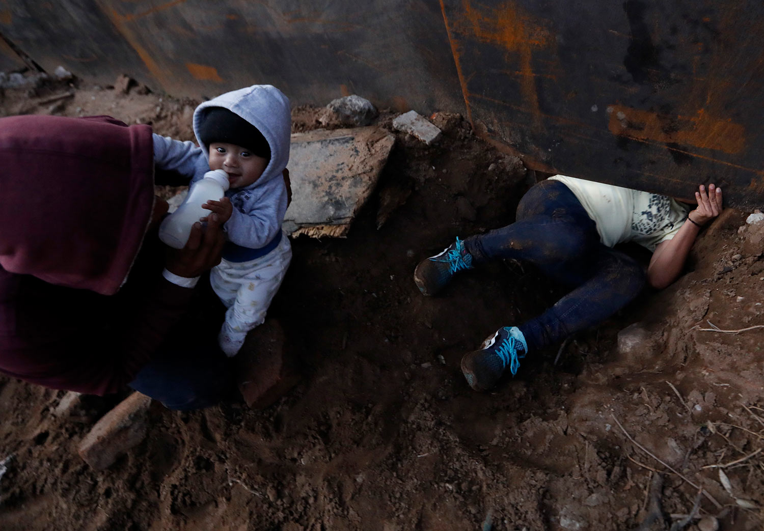  Honduran migrant Joel Mendez, 22, feeds his eight-month-old son Daniel as his partner Yesenia Martinez, 24, crawls through a hole under the U.S. border wall, in Tijuana, Mexico, Friday, Dec. 7, 2018. (AP Photo/Rebecca Blackwell) 