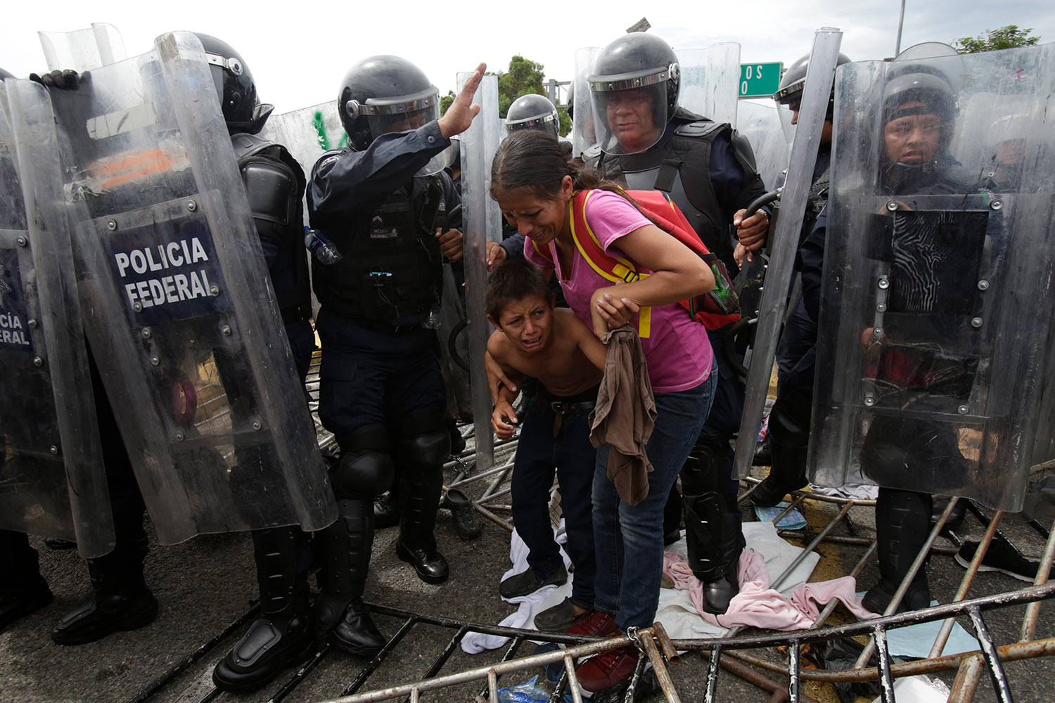  A Honduran migrant mother and child cower in fear as they are surrounded by Mexican Federal Police in riot gear, at the border crossing in Ciudad Hidalgo, Mexico, Friday, Oct. 19, 2018.  (AP Photo/Moises Castillo) 