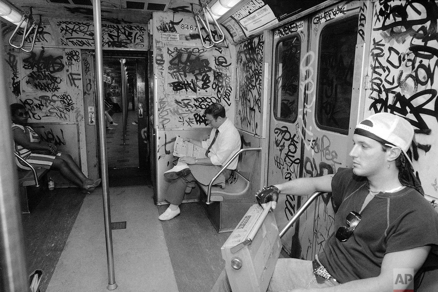  New York City Transit Police Officer Jeremiah Lyons, center, as a decoy cop reads his newspaper on board the city subway while he carries on his act as a fare-paying passenger wearing visible gold jewelry on July 25, 1985. His backup Police Officer 