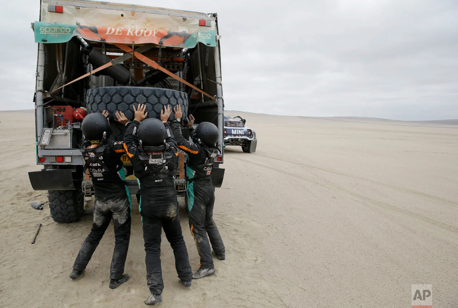 Driver Federico Villagra and co-drivers Arturo Yacopini and Ricardo Torlaschi, all of Argentina, lift a tyre onto their Iveco truck during the stage eight of the Dakar Rally between San Juan de Marcona and Pisco, Peru, Jan. 15, 2019. (AP Photo/Ricardo Mazalan)