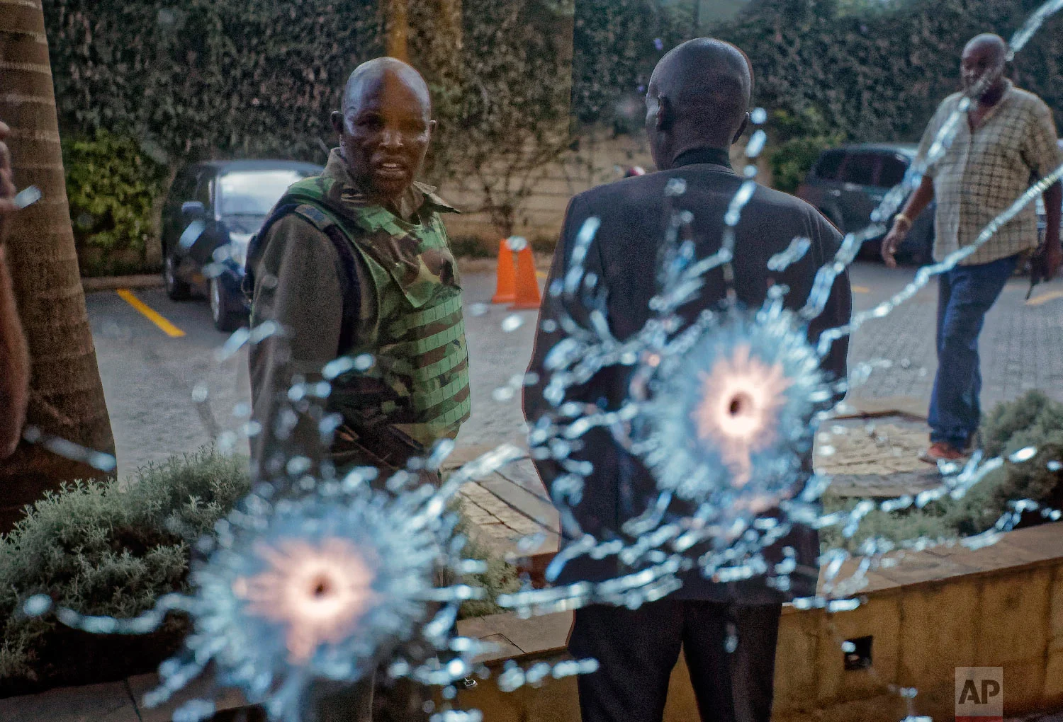 A member of the security forces is seen reflected in a window as he looks at bullet-holes, at a hotel complex in Nairobi, Kenya, Jan. 15, 2019. (AP Photo/Ben Curtis)