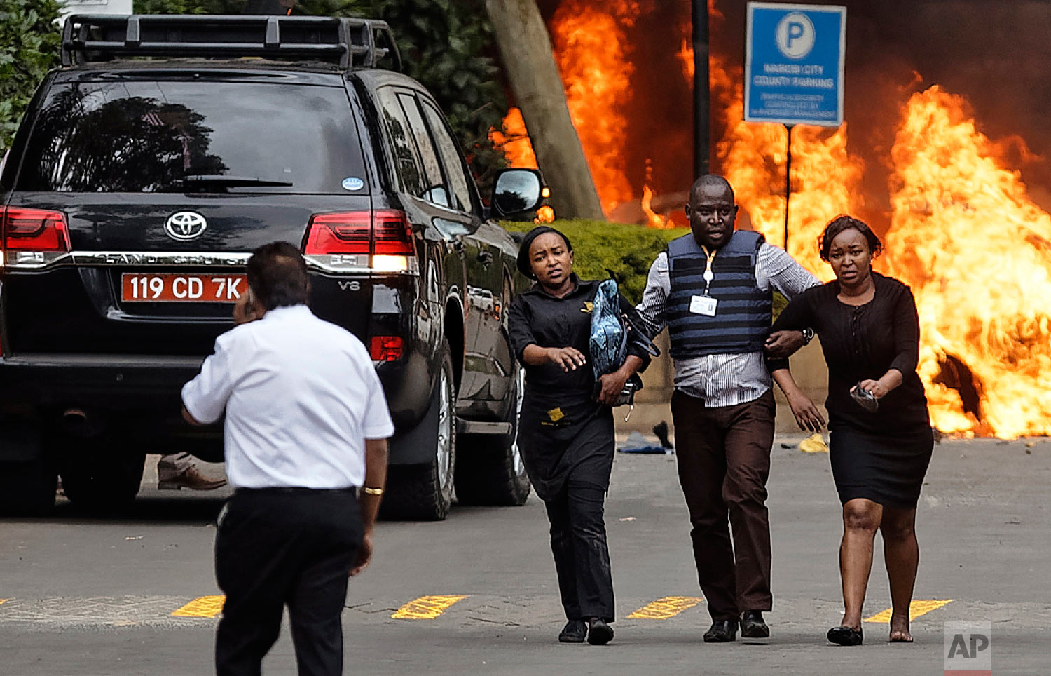 Security forces help civilians flee the scene as cars burn behind, at a hotel complex in Nairobi, Kenya Tuesday, Jan. 15, 2019. (AP Photo/Ben Curtis)