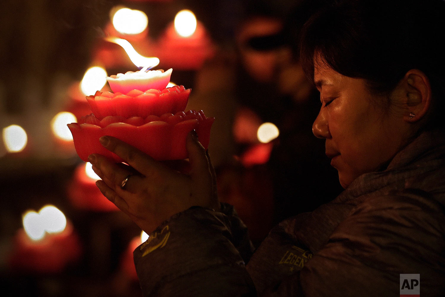  A woman holds a flower-shape candle prays on the first day of the Chinese Lunar New Year at the Tanzhe temple in the Mentougou District of Beijing, Tuesday, Feb. 5, 2019. (AP Photo/Andy Wong) 
