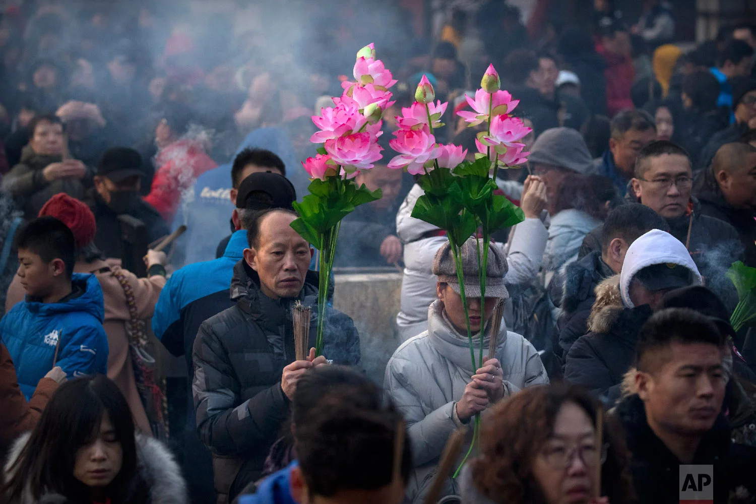 People hold floral bouquets and sticks of incense as they pray at the Lama Temple in Beijing, Tuesday, Feb. 5, 2019. (AP Photo/Mark Schiefelbein)