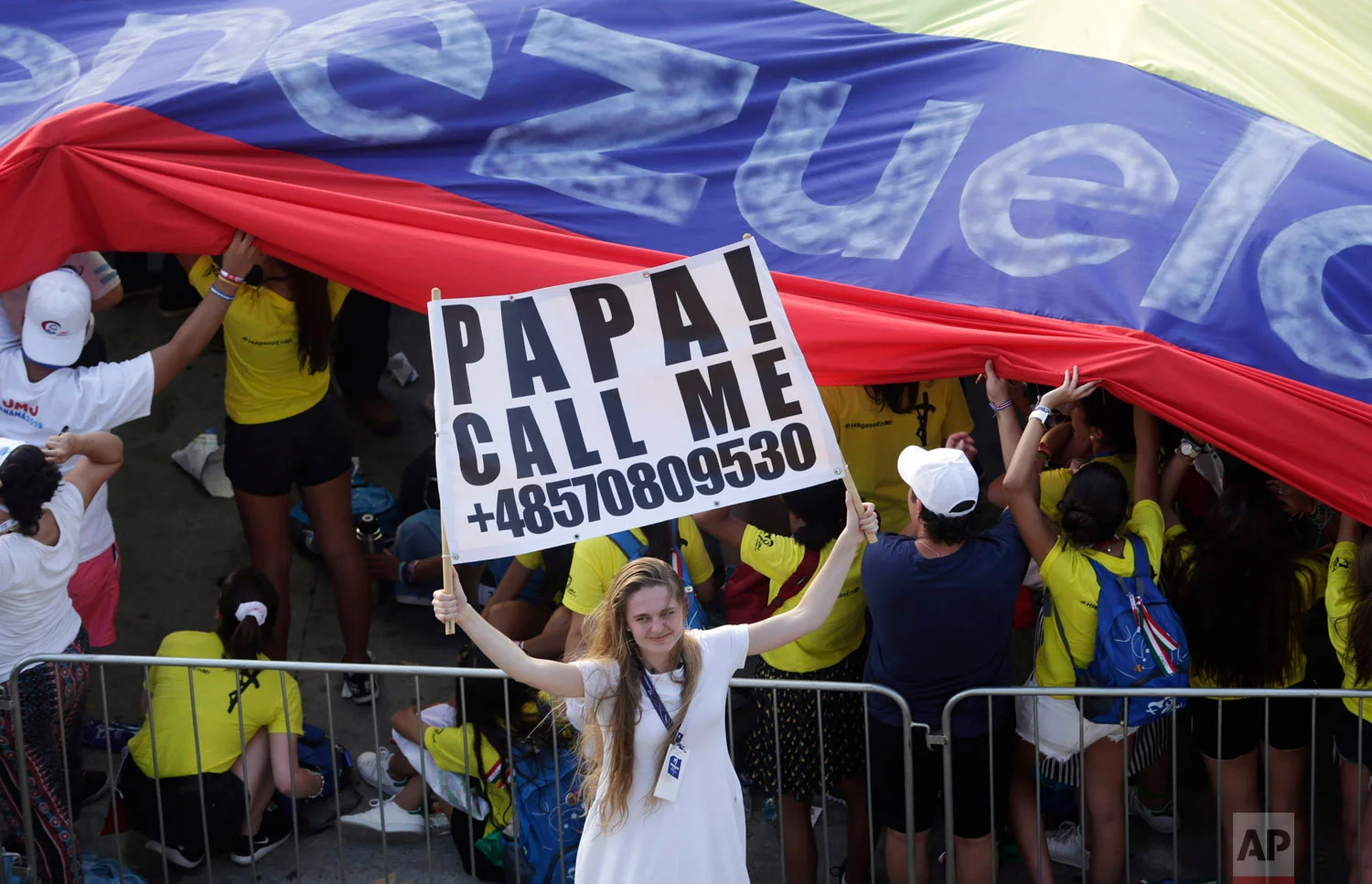 A young woman holds a sign asking Pope Francis to call her as she waits for him to arrive for an outdoor Mass in Panama City, Jan. 24, 2019. (AP Photo/Arnulfo Franco)
