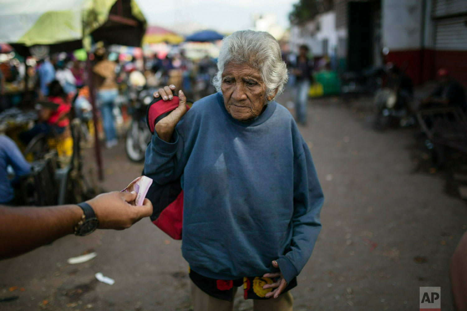  An elderly woman is offered cash as she begs at a wholesale food market in Caracas, Venezuela, Jan. 28, 2019. Economists agree that the longer the standoff between a U.S.-backed opposition leader and the president drags on, the more regular Venezuel