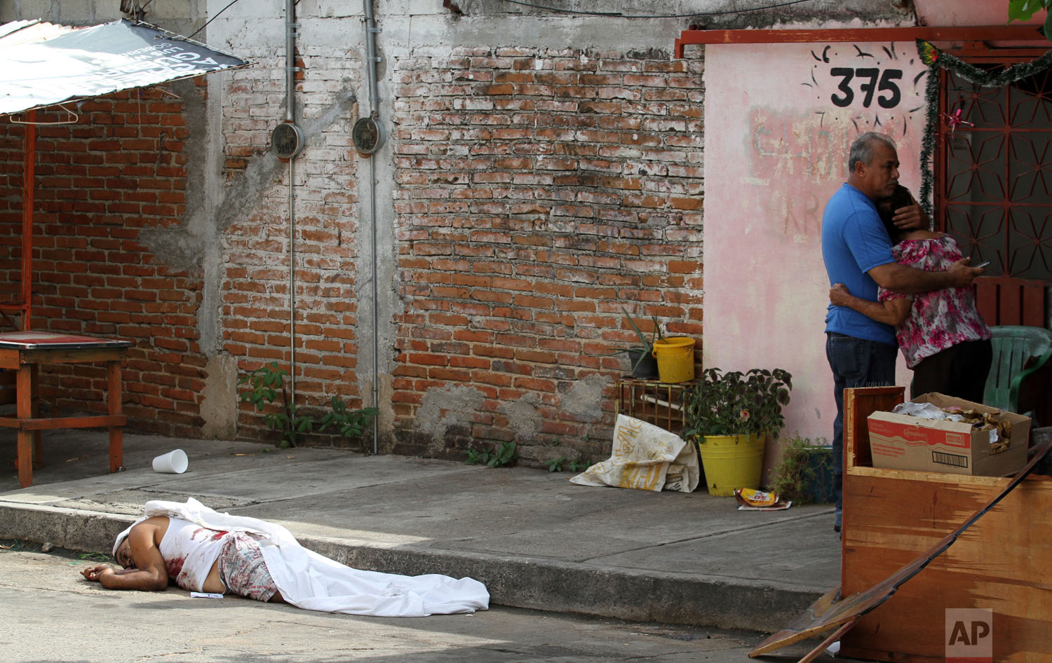  A man's body lies on the pavement after he was shot to death, as his parents hug nearby in Acapulco, Mexico, Jan. 2, 2019. (AP Photo/Bernardindo Hernandez) 