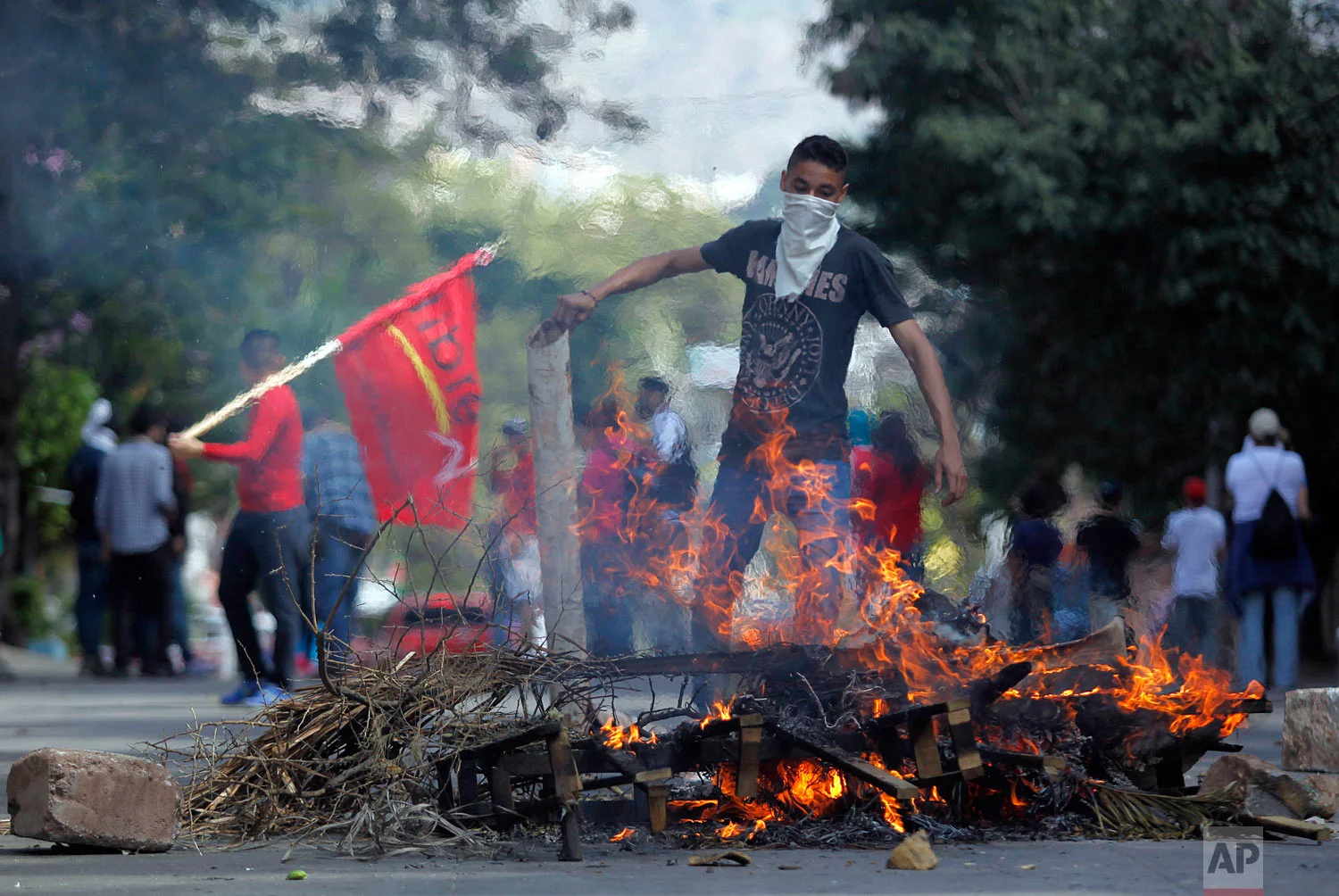 A masked demonstrator adds wood to a burning roadblock during a protest against the government of Honduras' President Juan Orlando Hernandez in Tegucigalpa, Honduras, Jan. 27, 2019, on the anniversary of Hernandez's reelection. (AP Photo/Fernando Antonio)