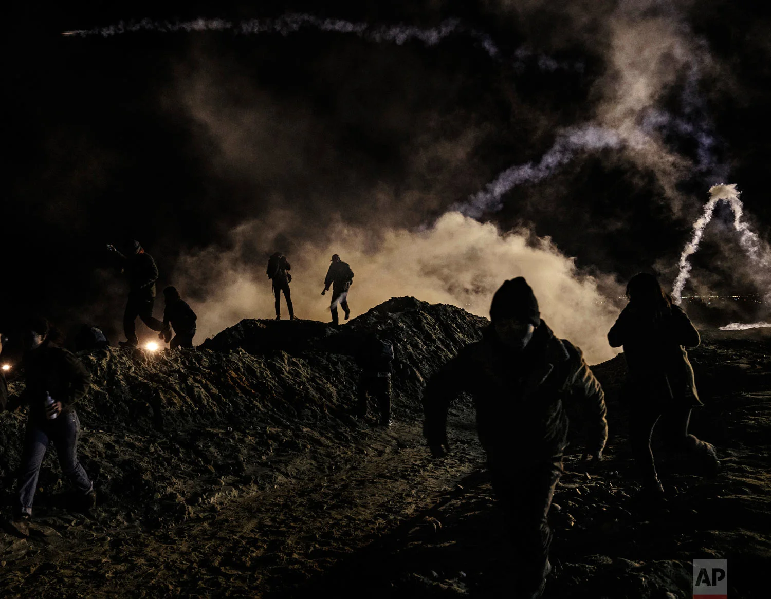 Migrants run from tear gas fired by U.S. Border Protection agents after they climbed the fence in an attempt to enter San Diego, Calif., from Tijuana, Mexico, Jan. 1, 2019. (AP Photo/Daniel Ochoa de Olza)