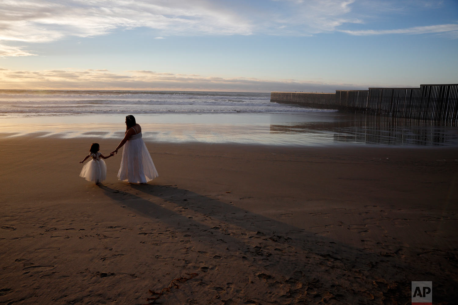  Ileze Dariel, of Tijuana, Mexico, reaches for the hand of her daughter Jimena as they wait for a photographer while taking family pictures on the beach next to the border wall, right, Jan. 9, 2019, in Tijuana, Mexico. (AP Photo/Gregory Bull) 