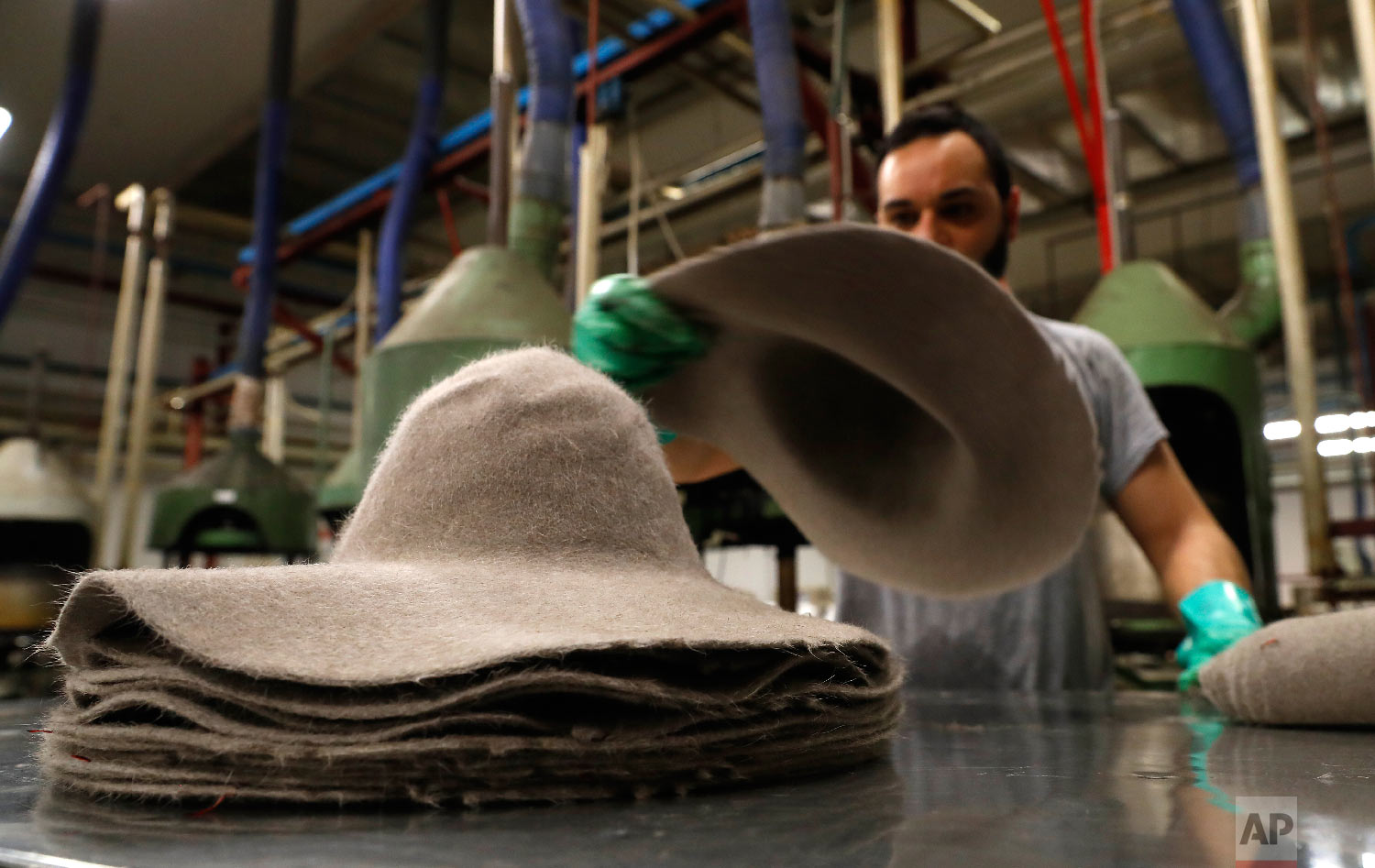 A man piles felt hats inside Borsalino's hat factory, in Spinetta Marengo, near Alessandria, Italy, Thursday, Jan. 17, 2019. (AP Photo/Antonio Calanni)