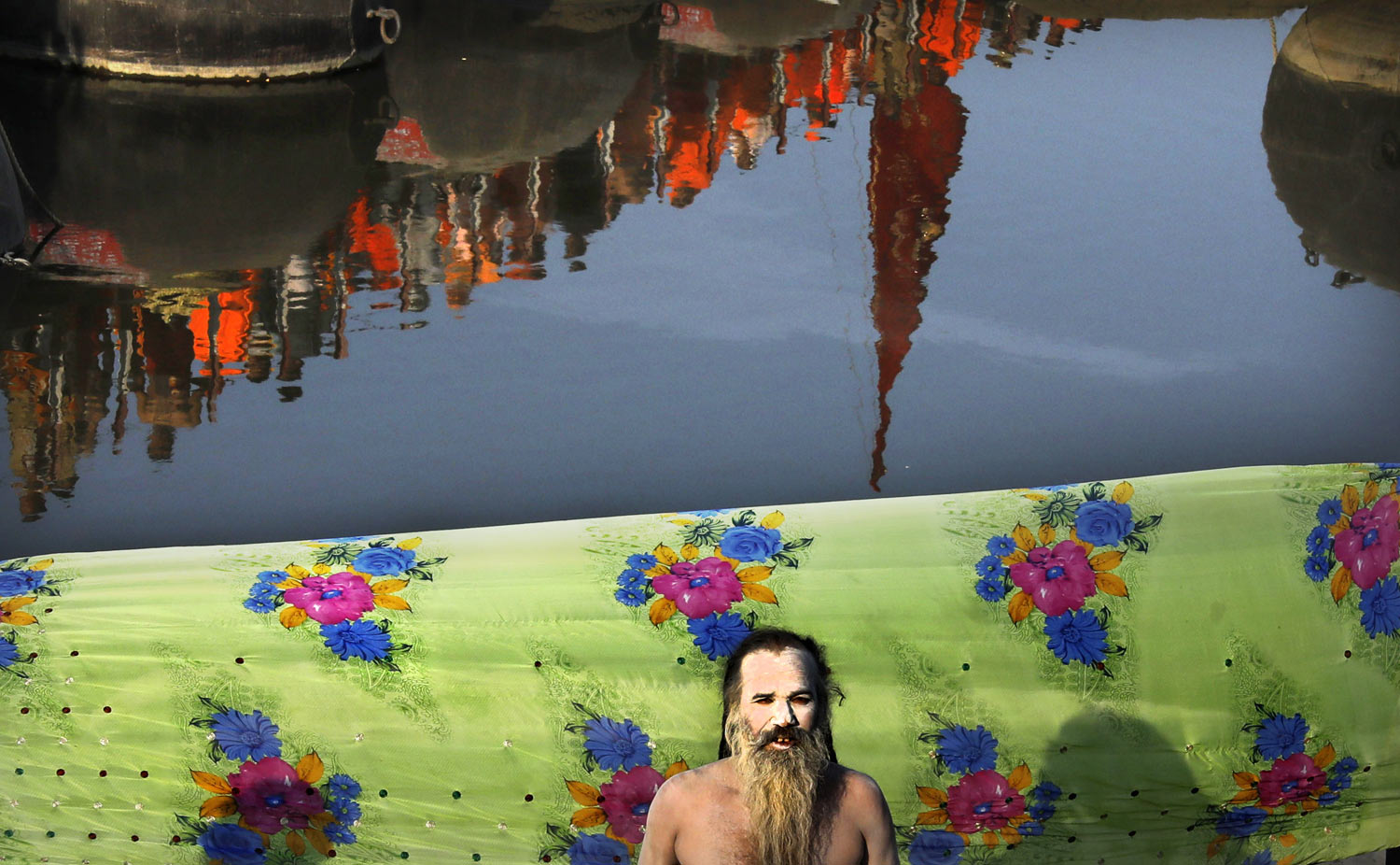 A naked Hindu holy man prays as others cross a pontoon bridge to take ritualistic dip on the auspicious day of Basant Panchami at Sangam, the confluence of sacred rivers the Yamuna, the Ganges and the mythical Saraswati, during the Kumbh Mela or the Pitcher Festival, in Prayagraj, Uttar Pradesh state, India, Sunday, Feb. 10, 2019. The Kumbh Mela is a series of ritual baths by Hindu sadhus, or holy men, and other pilgrims at Sangam that dates back to at least medieval times. Pilgrims bathe in the river believing it cleanses them of their sins and ends their process of reincarnation. (AP Photo/Rajesh Kumar Singh)