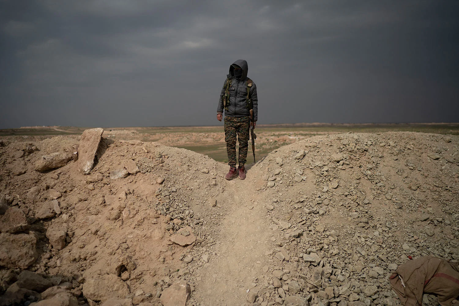 A U.S.-backed Syrian Democratic Forces (SDF) fighter stands atop a hill in the desert outside the village of Baghouz, Syria, Thursday, Feb. 14, 2019. (AP Photo/Felipe Dana)