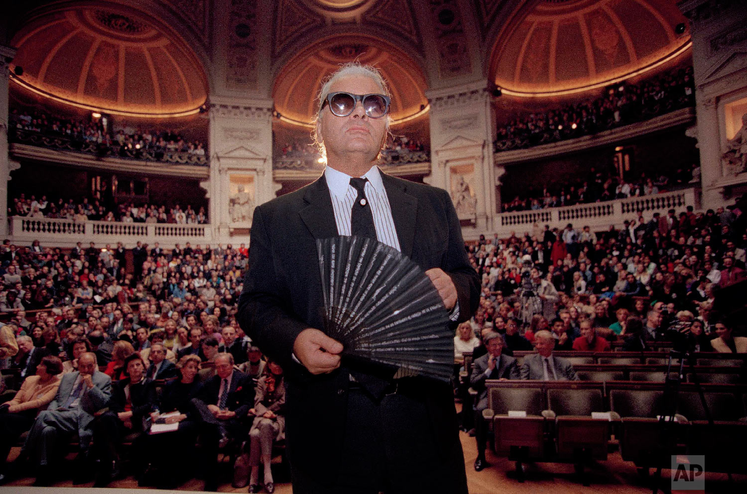 Karl Lagerfeld, the German fashion designer for Chanel, holds his fan as he enters the main auditorium at the Sorbonne, the oldest and most famous university in France, Oct. 18, 1994. (AP Photo/Lionel Cironneau)