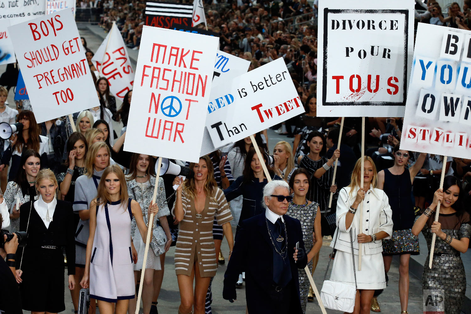 Models stage a fake demonstration, with German fashion designer Karl Lagerfeld, center right, as part of Chanel's Spring/Summer 2015 ready-to-wear fashion collection presented in Paris, France, Sept. 30, 2014. (AP Photo/Francois Mori)