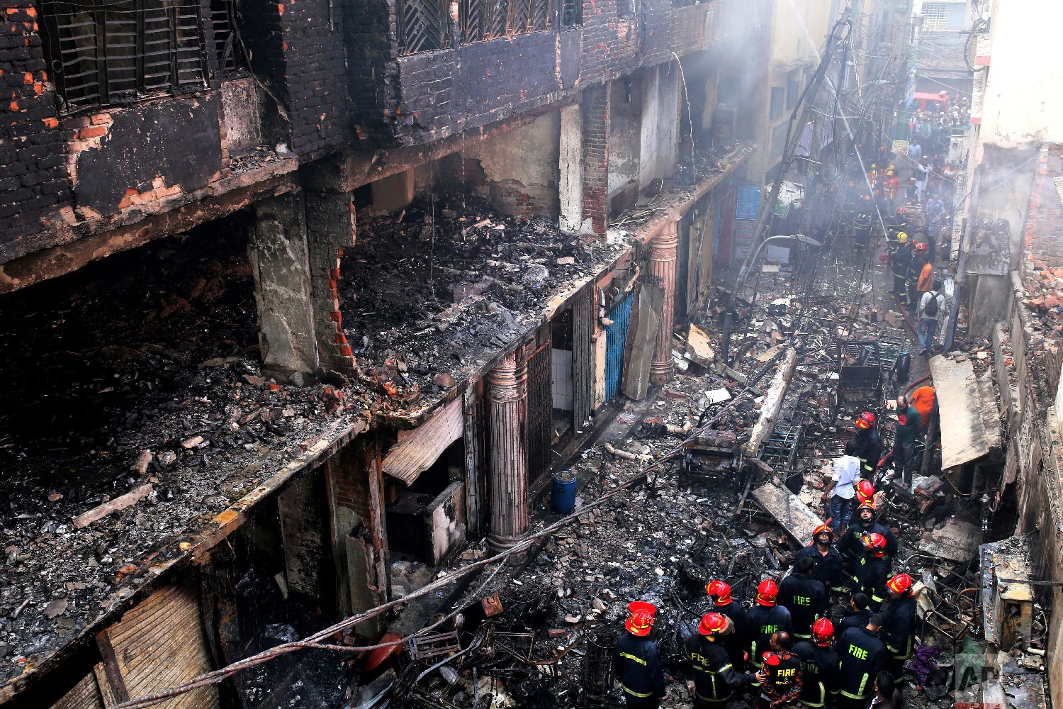 Locals and firefighters gather around buildings that caught fire late Wednesday in Dhaka, Bangladesh, Thursday, Feb. 21, 2019. (AP Photo/Rehman Asad)