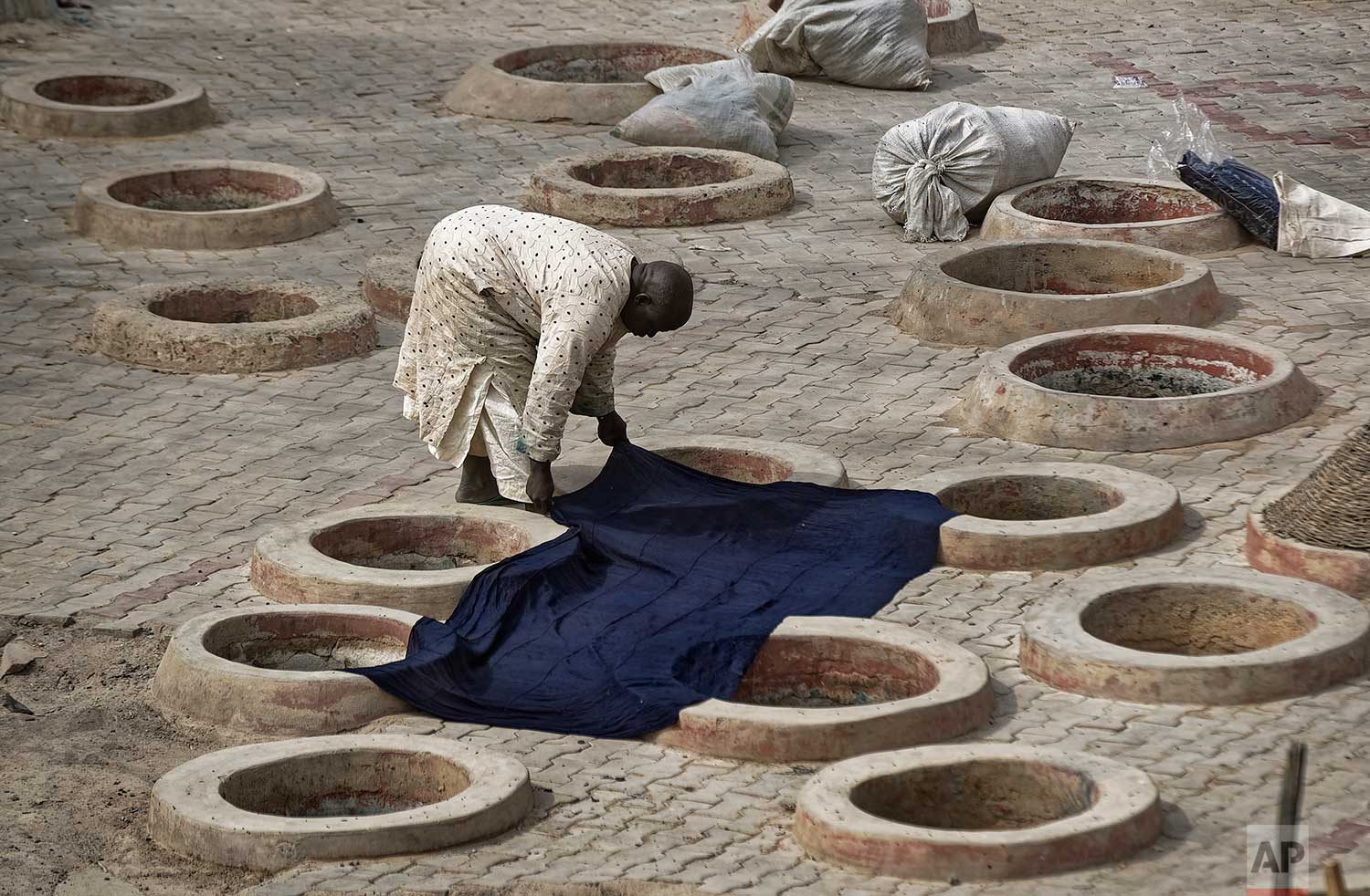  In this photo taken Tuesday, Feb. 19, 2019, a craftsman lays indigo-dyed cloth to dry over some of the ancient dye pits of Kofar Mata in Kano, northern Nigeria. (AP Photo/Ben Curtis) 