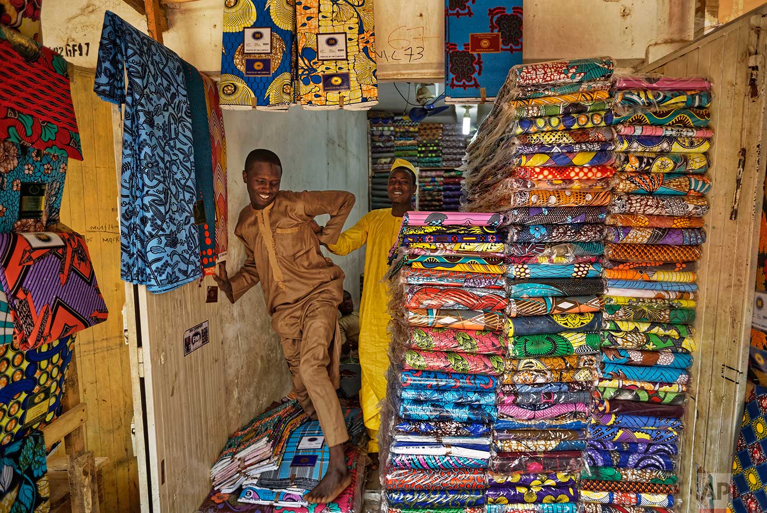  In this photo taken Tuesday, Feb. 19, 2019, shopkeepers stand by stacks of the wax-printed fabric made in China that fills the market in Kano, northern Nigeria. (AP Photo/Ben Curtis) 