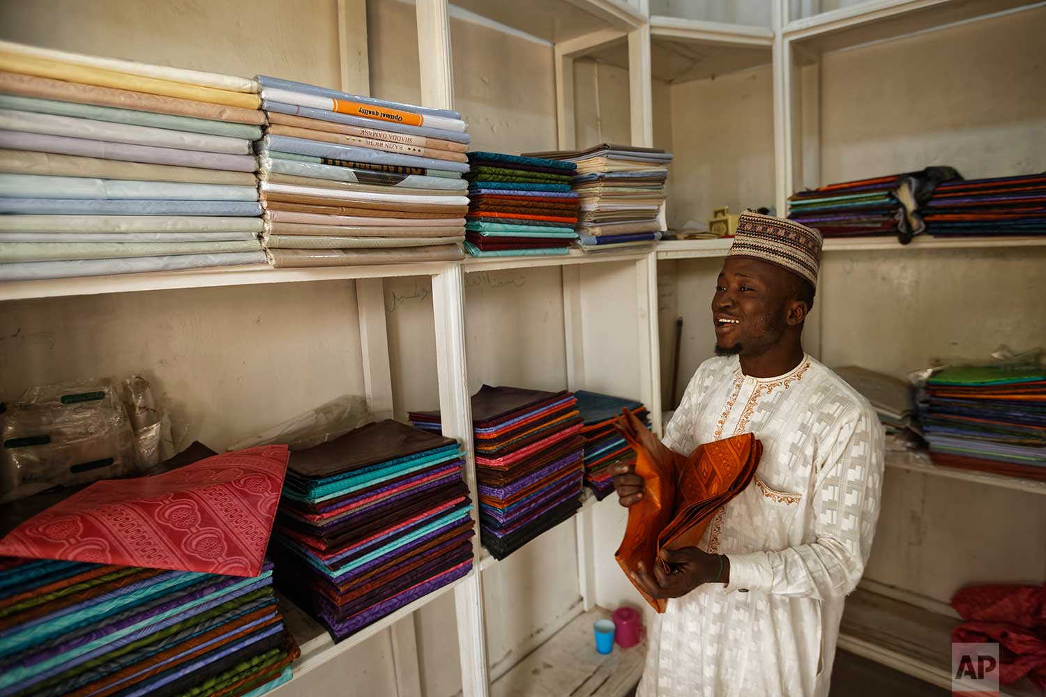  In this photo taken Tuesday, Feb. 19, 2019, a shopkeeper sells dyed fabric made in China at his stall in the market in Kano, northern Nigeria. (AP Photo/Ben Curtis) 