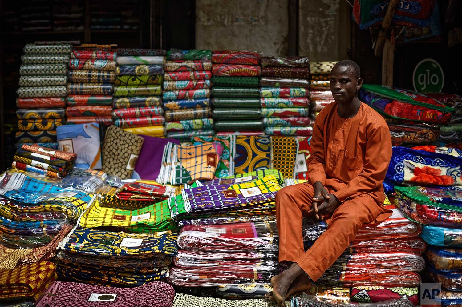 In this photo taken Tuesday, Feb. 19, 2019, a shopkeeper sits at his stall selling a variety of wax-printed fabrics made in China that fill the market in Kano, northern Nigeria. (AP Photo/Ben Curtis)