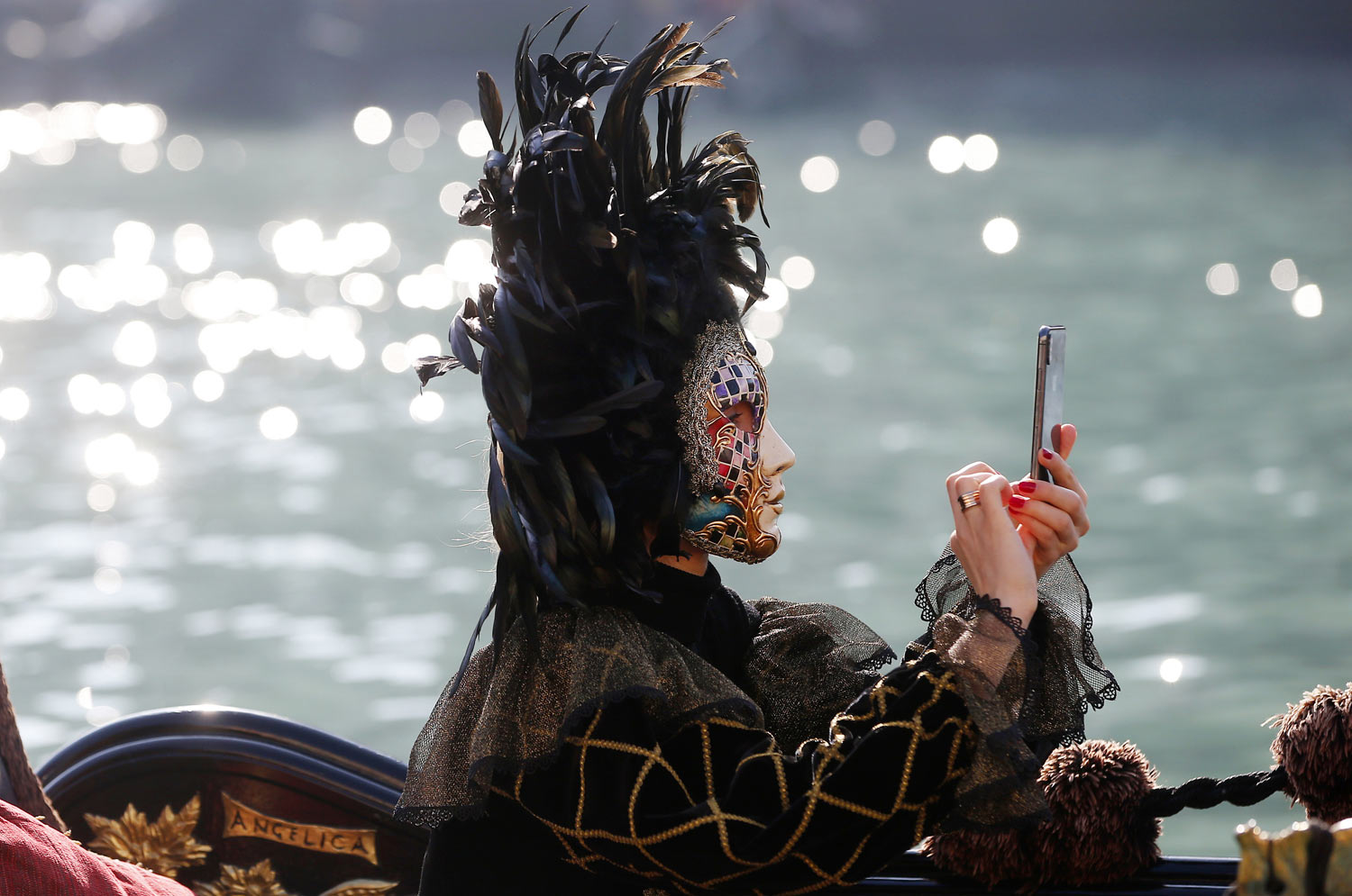 A masked woman checks her smartphone as she sits in a gondola during the water parade of the Venice Carnival in Venice, Italy, Sunday, Feb. 17, 2019. The event in the historic lagoon city attracts people from around the world. (AP Photo/Antonio Calanni)