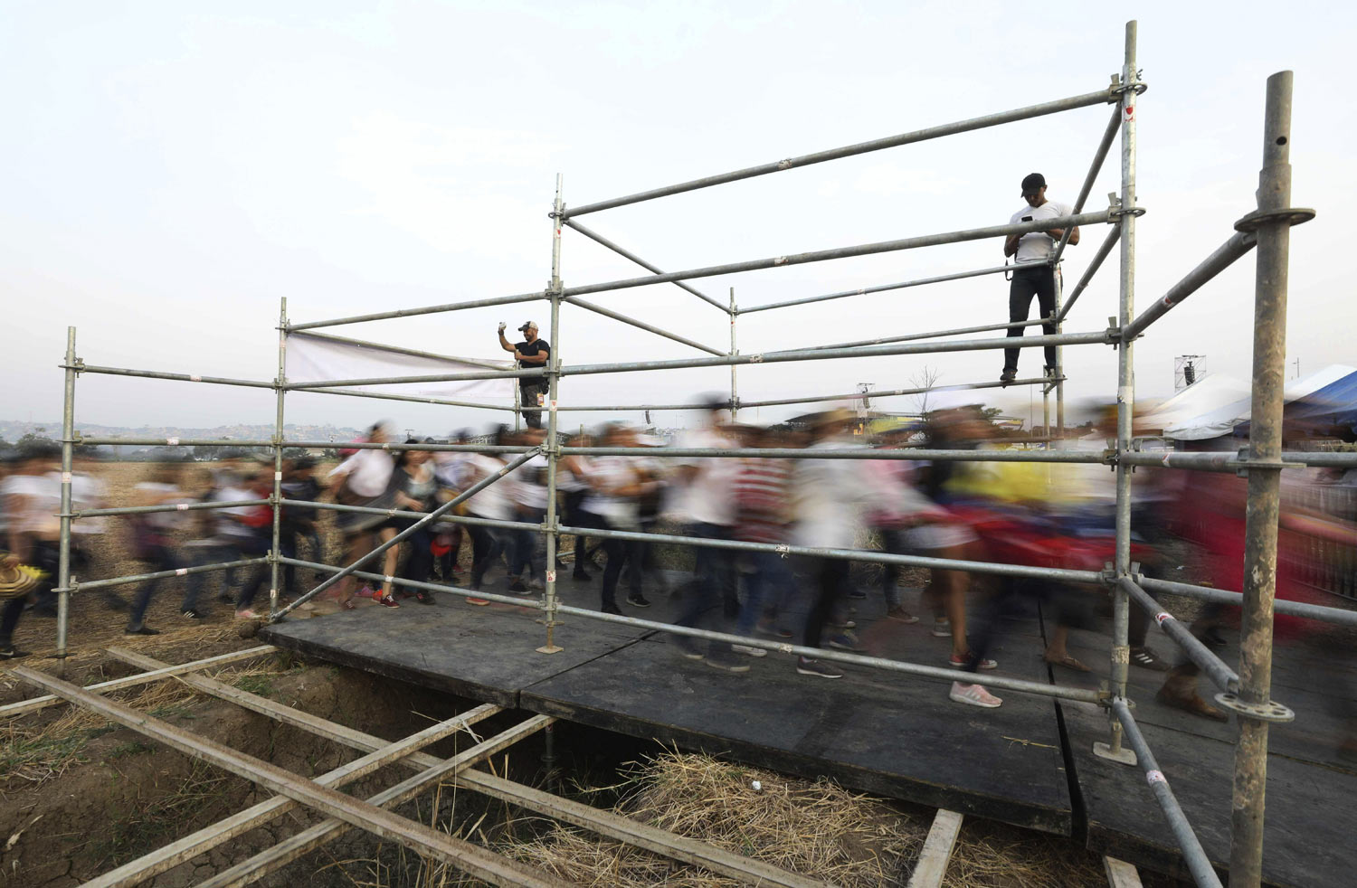 People stream through a gate before the Venezuela Aid Live concert on the Colombian side of Tienditas International Bridge on the outskirts of Cucuta, Colombia, on the border with Venezuela, Friday, Feb. 22, 2019. Venezuela's power struggle is set to convert into a battle of the bands Friday when musicians demanding Nicolas Maduro allow in humanitarian aid and those supporting the embattled leader's refusal sing in rival concerts being held at both sides of a border bridge where tons of donated food and medicine are being stored. (AP Photo/Fernando Vergara)